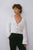 Woman wearing Aje Grooves Lace Stitch Cardigan in white coming in cropped length, with V-neckline, adorned with gold shell buttons, beautiful balloon sleeves and ribbed cuffs.