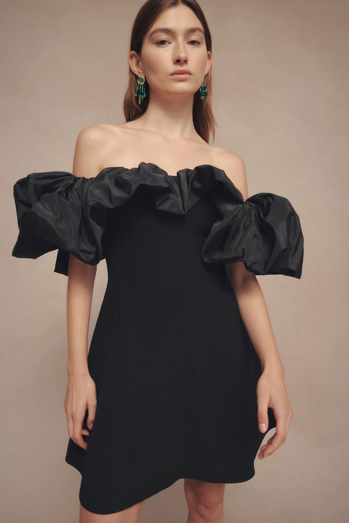 Woman wearing Eldora Mini Black Dress from Aje with fitted waist and flared skirt, featuring controlled volume puff neck and sleeve, achieved through a woven elasticated design.