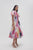 Woman wearig Aje Nova Pleated Midi Dress with splashed patterns of pink, blue, purple, and grey contrasting to white backdrop.
